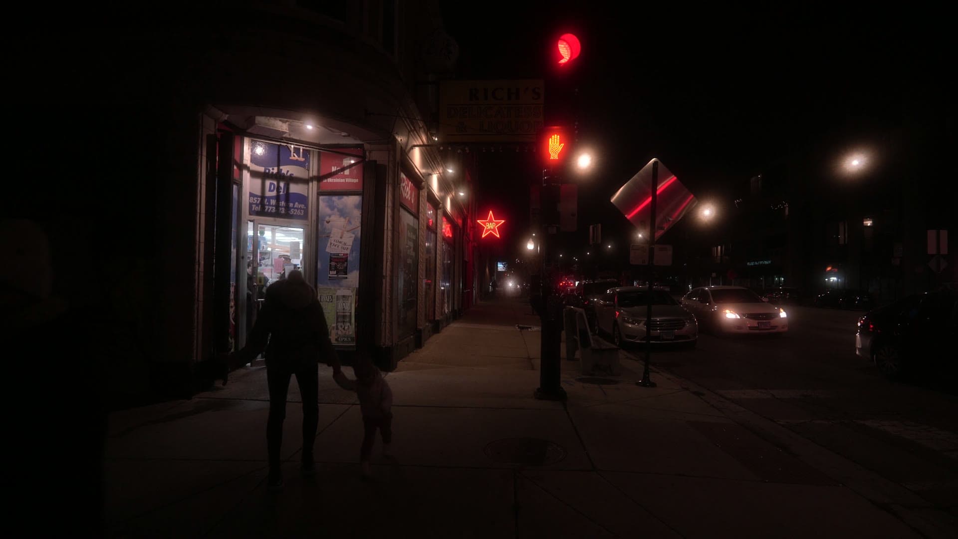 A neighborhood street at dusk lit by the red neon of an old corner tavern